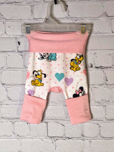 Front: White pants with pink and purple small hearts. Larger hearts of purple, teal and pink mixed in with baby Mickey and Minnie Mouse and Pluto. Soft pink waistband folded down and leg bands folded up for smaller size