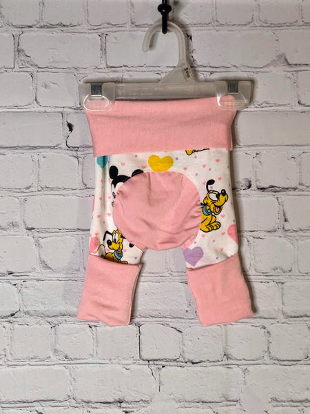 Back: White pants with pink and purple small hearts. Larger hearts of purple, teal and pink mixed in with baby Mickey and Minnie Mouse and Pluto. Soft pink waistband folded down and leg bands folded up for smaller size. Bum circle of soft pink.